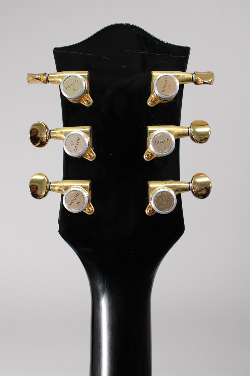 Rear view of the black headstock and neck, showing six gold-plated tuning machines with light wear and minor scratches on the finish.