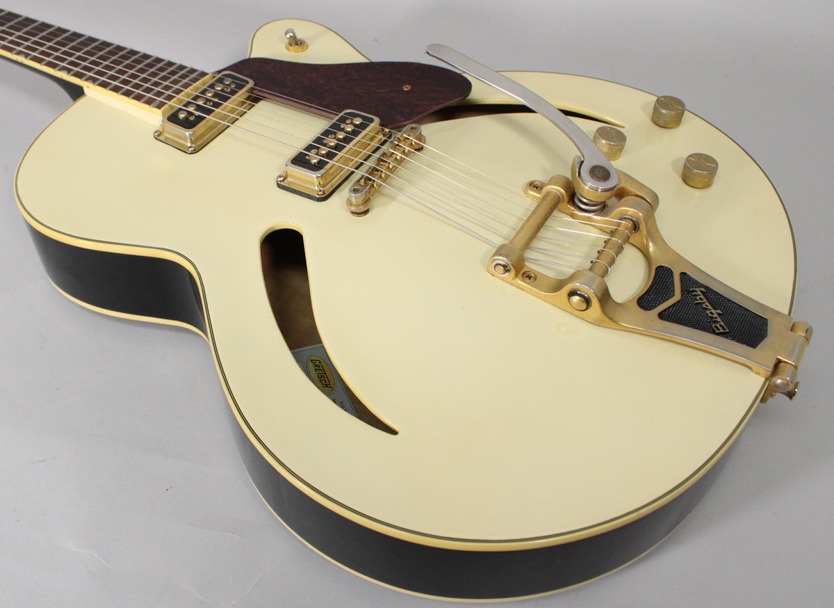Close-up of the antique white hollow body with black sides, showing gold hardware, two humbuckers, a Bigsby tremolo, and f-holes.