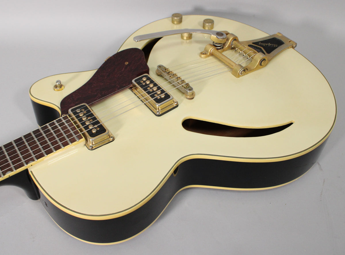 Cream hollow-body electric guitar, angled from the neck, showing gold hardware, f-hole, and dark pickguard.
