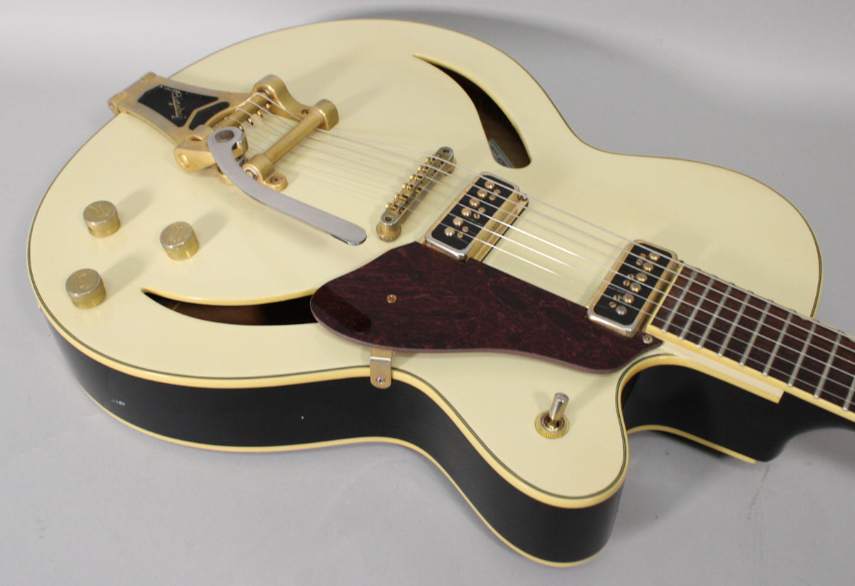 Upper body of an antique white hollow-body guitar with gold hardware, Bigsby tremolo, f-holes, and a dark red pickguard.