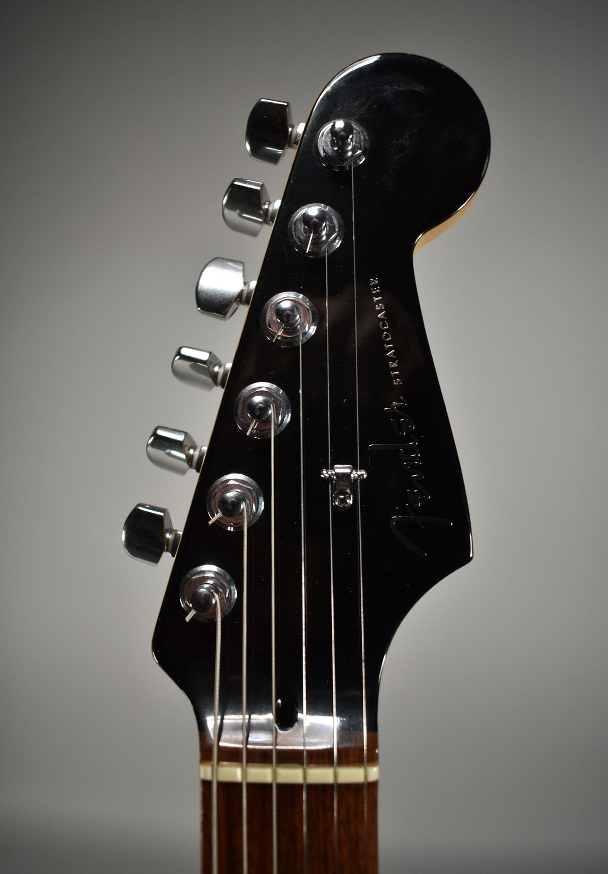 Close-up of the glossy black headstock with six chrome tuners and a string tree, showing light surface scratches.