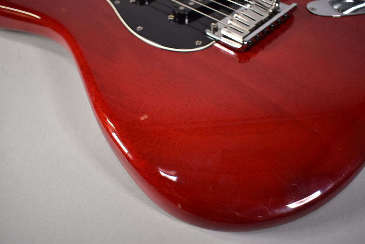 The crimson red Stratocaster body, with visible wood grain, shows light scratches and a small ding near the lower horn.