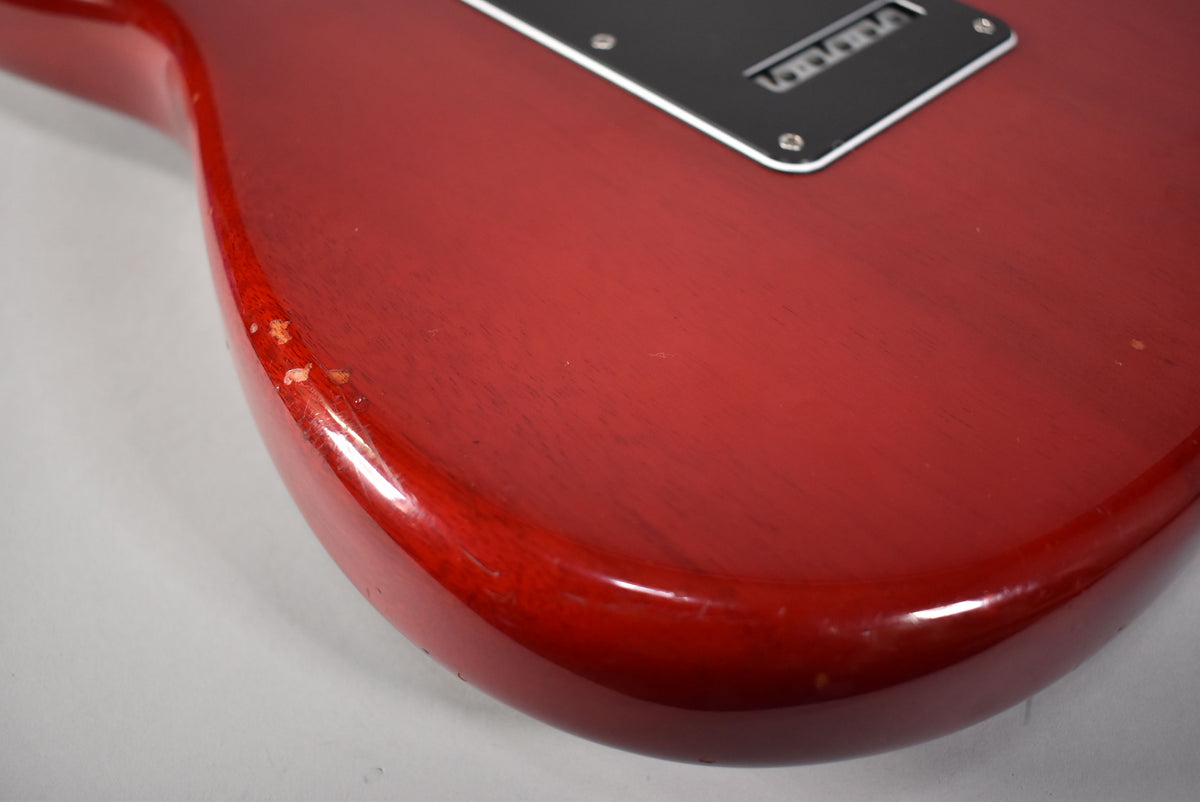 Close-up of the crimson red Stratocaster's lower bout, showing finish chips on the edge and light scratches on the back plate.