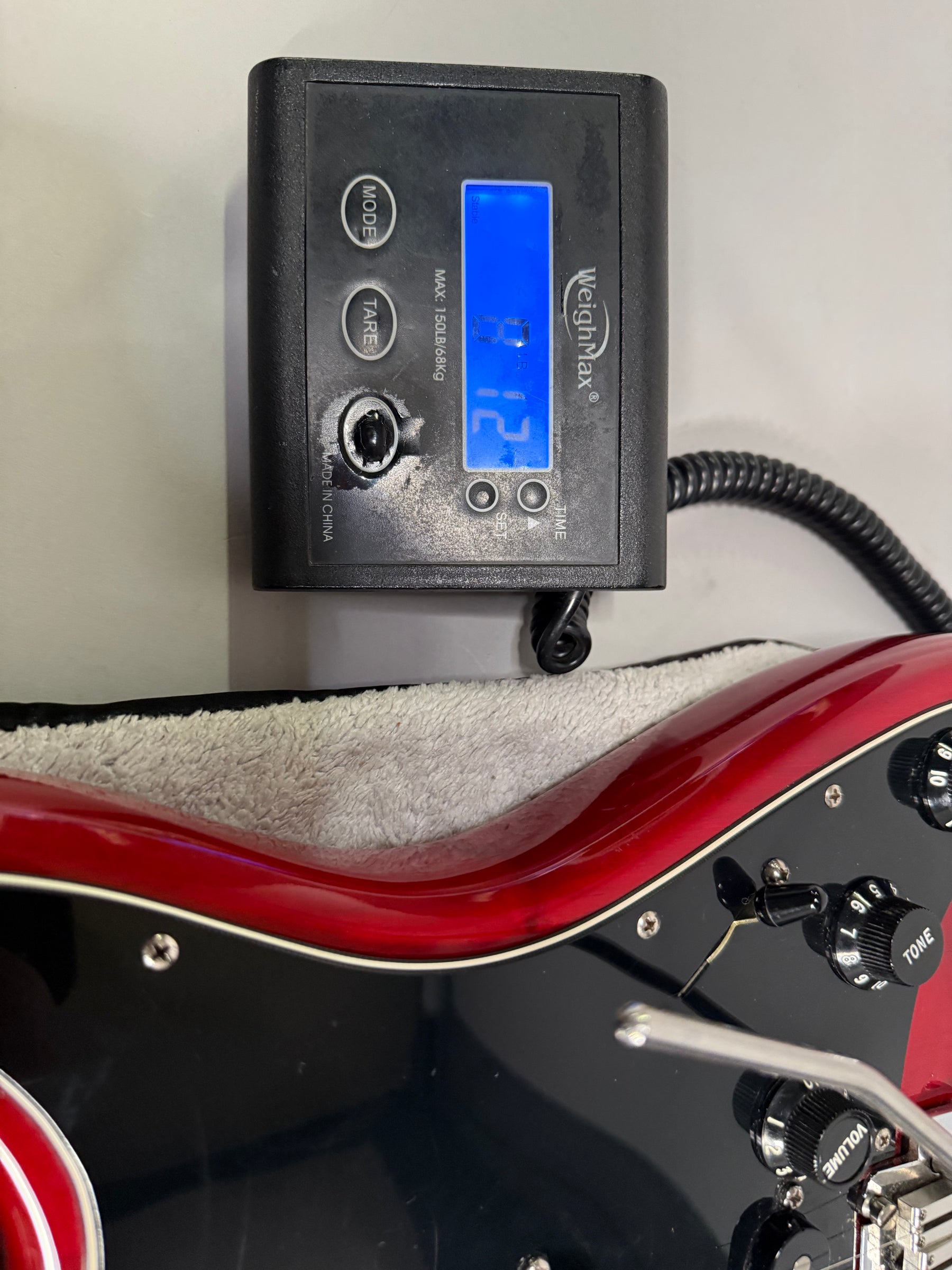 The crimson red Stratocaster body, with a black pickguard and controls, is partially visible below a digital scale displaying "8.12".