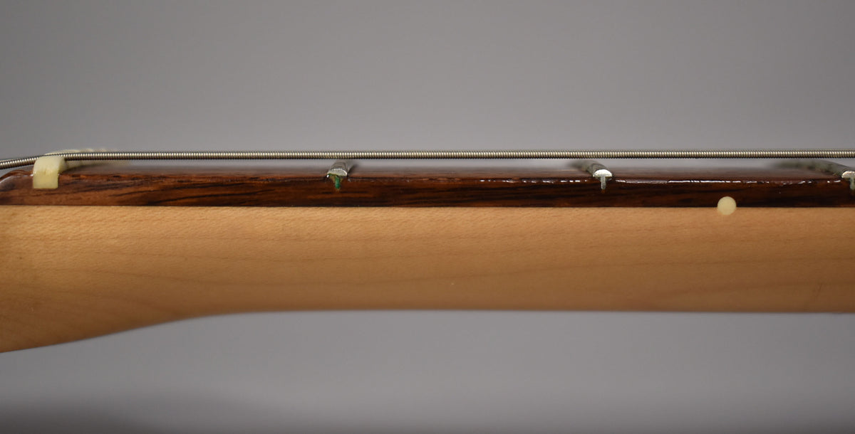 Close-up of the guitar's neck, showing the dark rosewood fretboard, light maple neck, and strings over a cream nut.