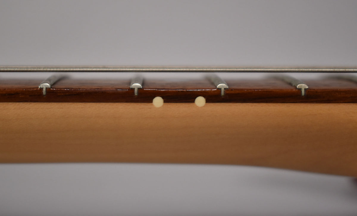 Close-up of the guitar's dark brown fretboard and light maple neck, showing two cream side dots and four frets with strings.