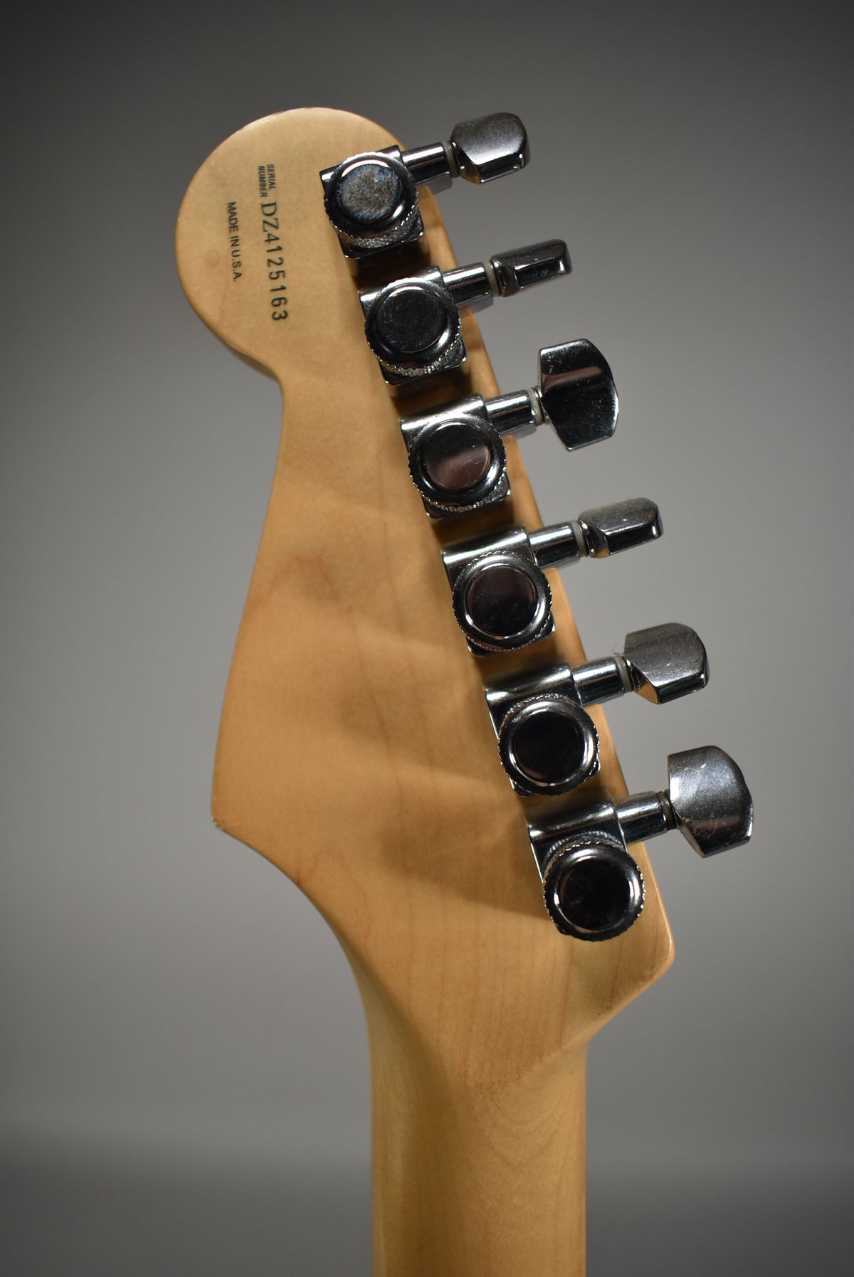 The back of the guitar's light wood headstock and neck, showing six chrome tuners with light wear and a serial number stamp.
