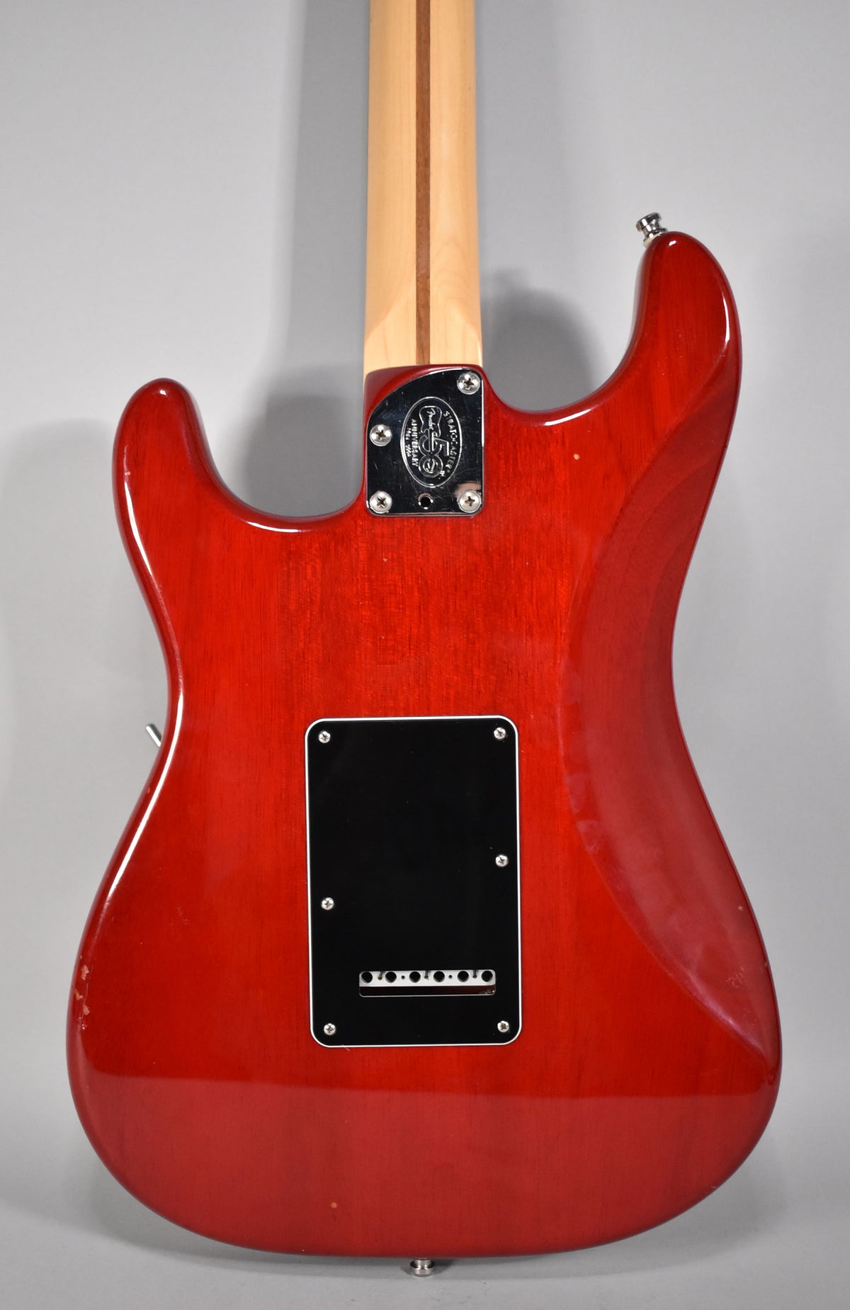 Rear view of a crimson red Stratocaster, showing the mahogany grain, a black tremolo cover, and a chrome neck plate.