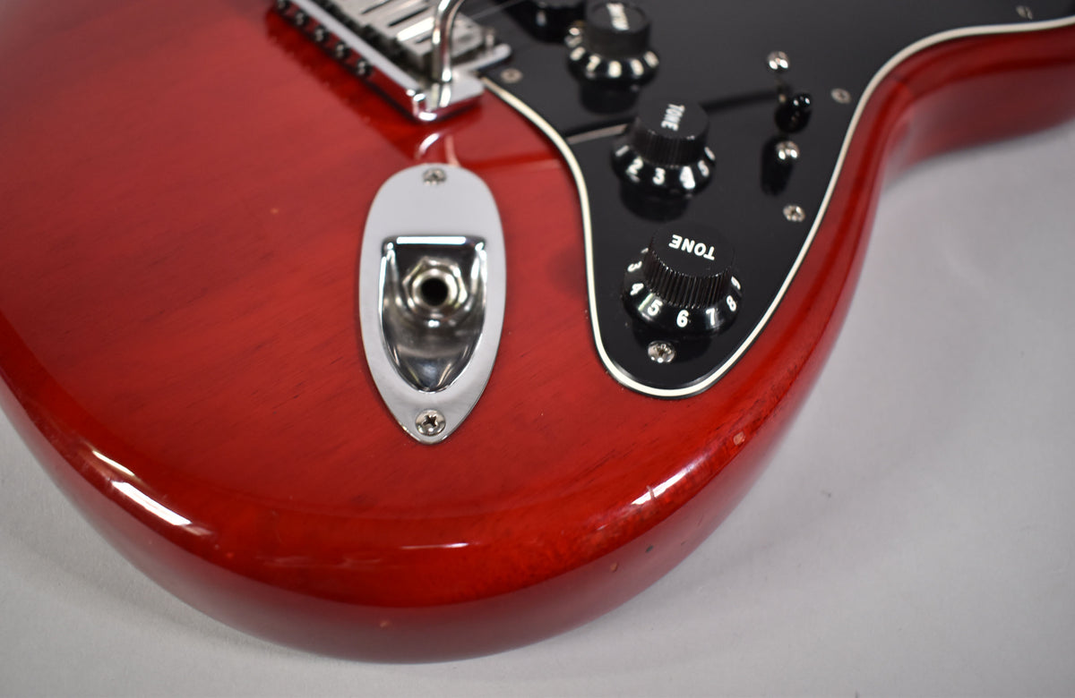 Close-up of the crimson red body, showing the chrome output jack, black pickguard with three black control knobs, and minor wear on the edge.