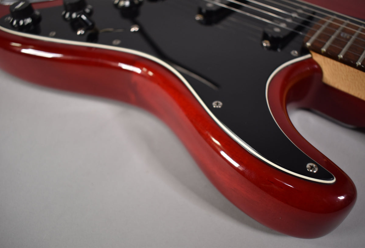 Close-up of the crimson red body and black pickguard, showing the lower horn and control knobs, with a hint of the fretboard.
