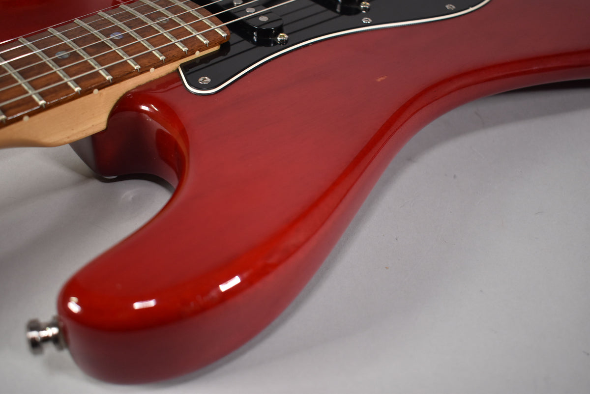 Close-up of the crimson red Stratocaster body, showing the lower horn, output jack, black pickguard, and some minor finish wear.