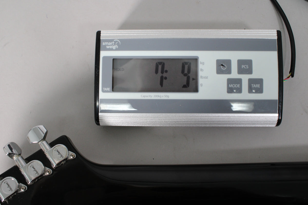 The black guitar's headstock and tuning pegs are visible in the foreground, with a digital scale displaying "7.9" in the background.
