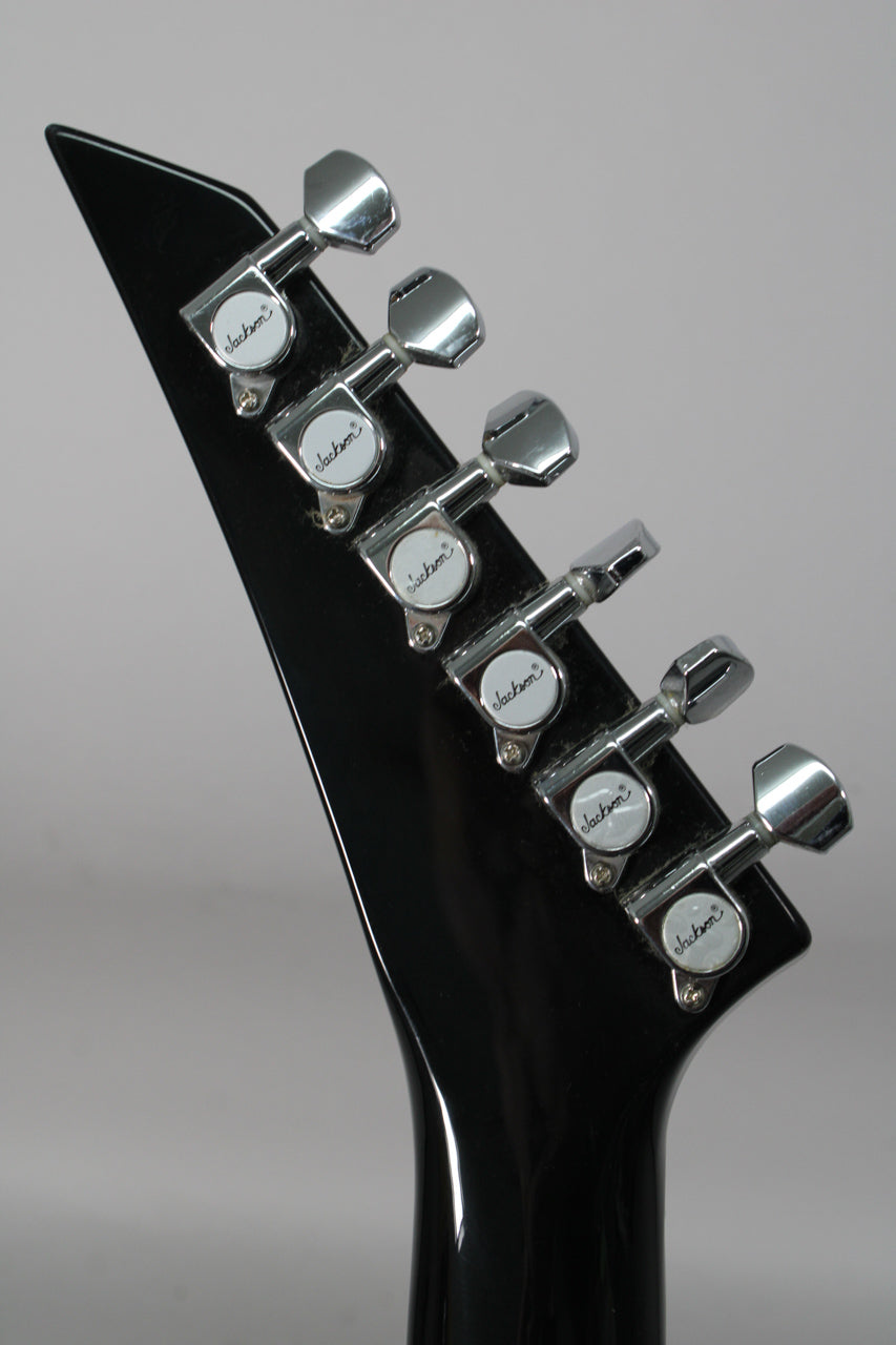 Angled close-up of the black gloss headstock and neck joint, showing six chrome tuners with white pearloid buttons.