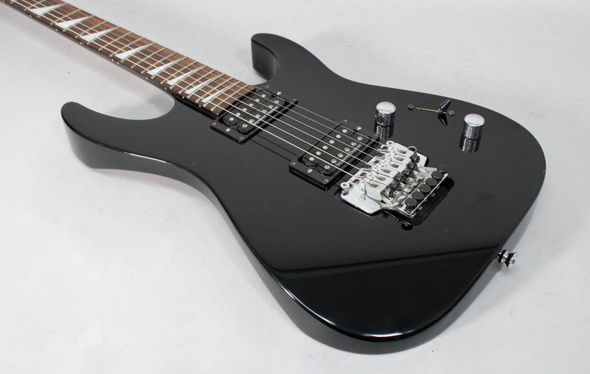 Black electric guitar, angled from above, showing the body with two humbuckers, a chrome Floyd Rose bridge, and two knurled chrome knobs.