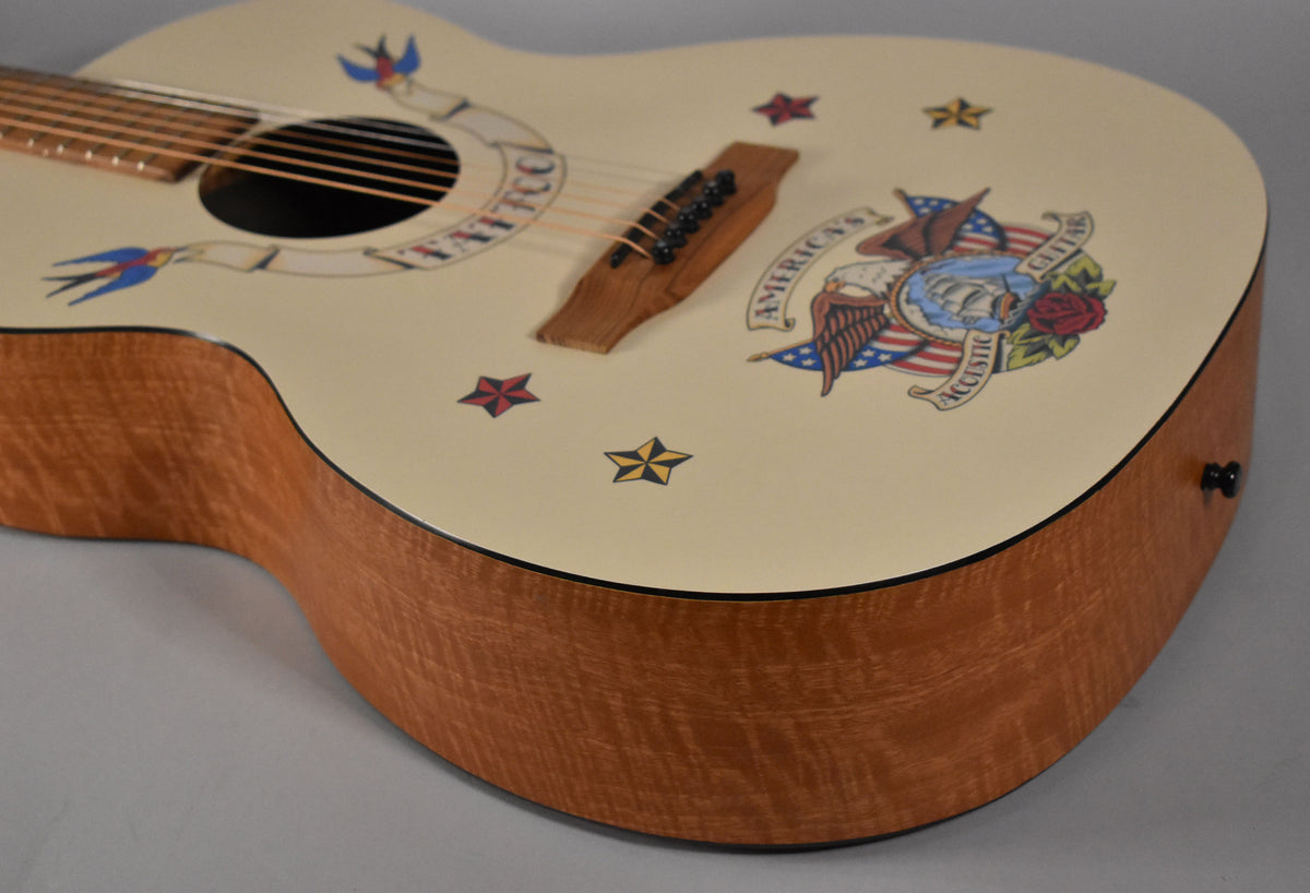 The cream-colored acoustic guitar body, with a natural wood grain side, features colorful tattoo-style decals.