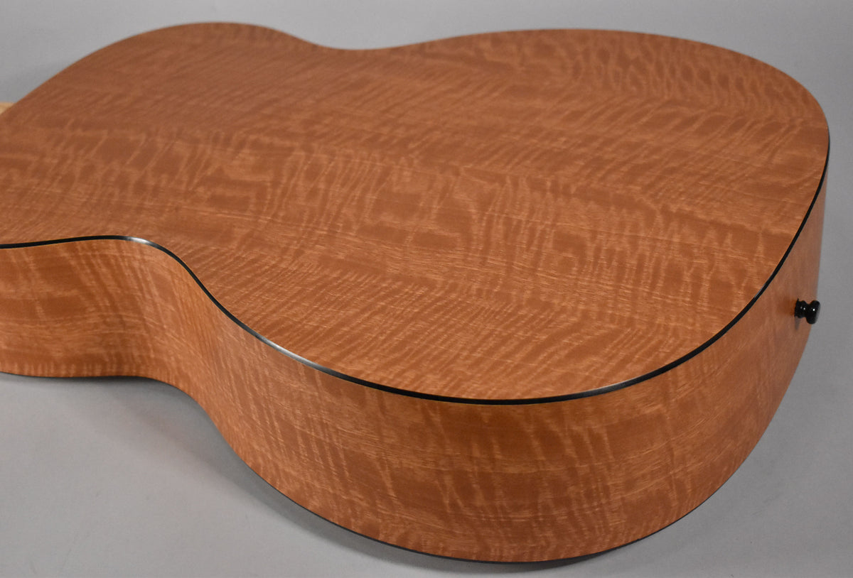 The back and lower bout of the acoustic guitar, showing its figured maple wood grain and black binding, with a black endpin.