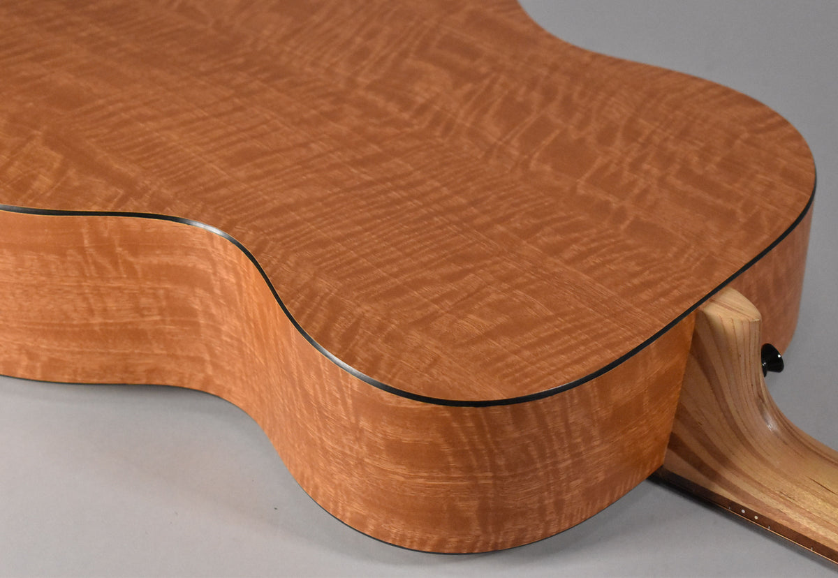 The guitar's lower bout and waist are angled from above, revealing a light brown, wavy-grained wood with black binding.