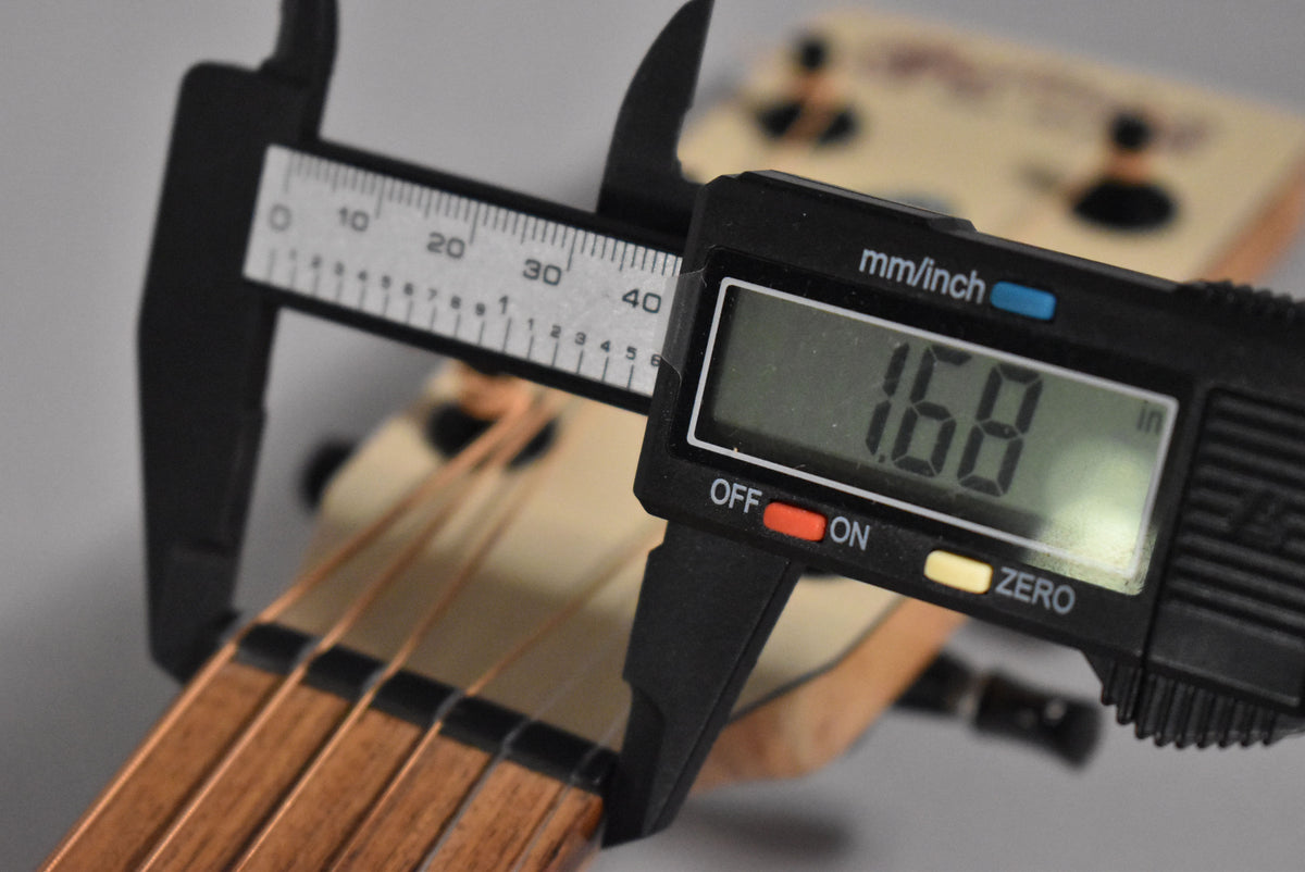 A digital caliper measures the nut width of the guitar at 1.68 inches, with the fretboard and strings visible.
