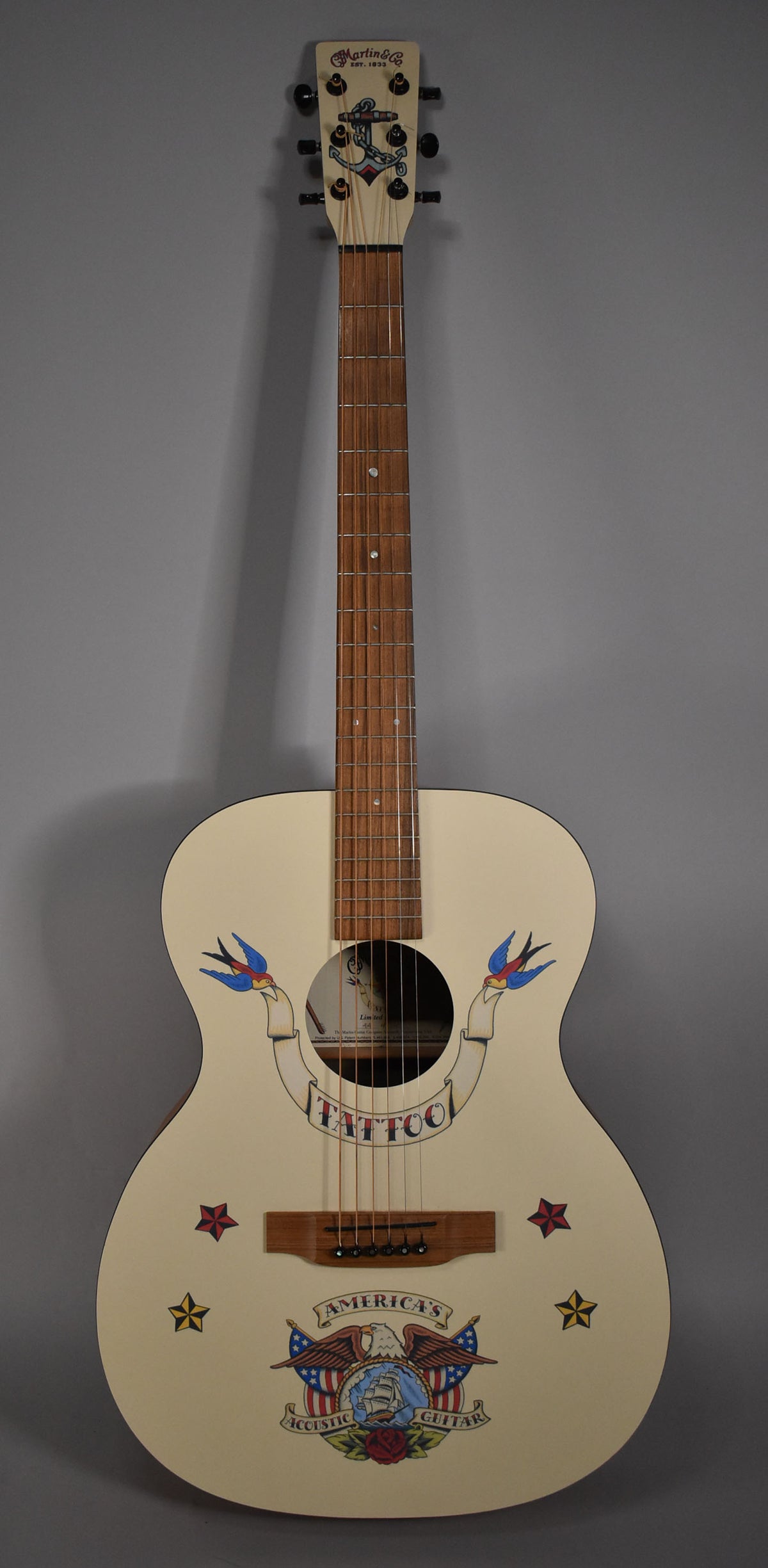 Full front view of a cream acoustic guitar with a light brown fretboard, featuring colorful tattoo-style decals.