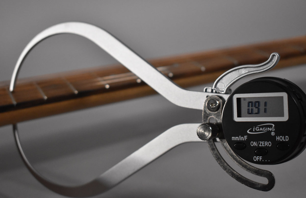 A digital caliper measures the guitar's dark brown fretboard, showing a reading of 0.91, with white fret markers visible.