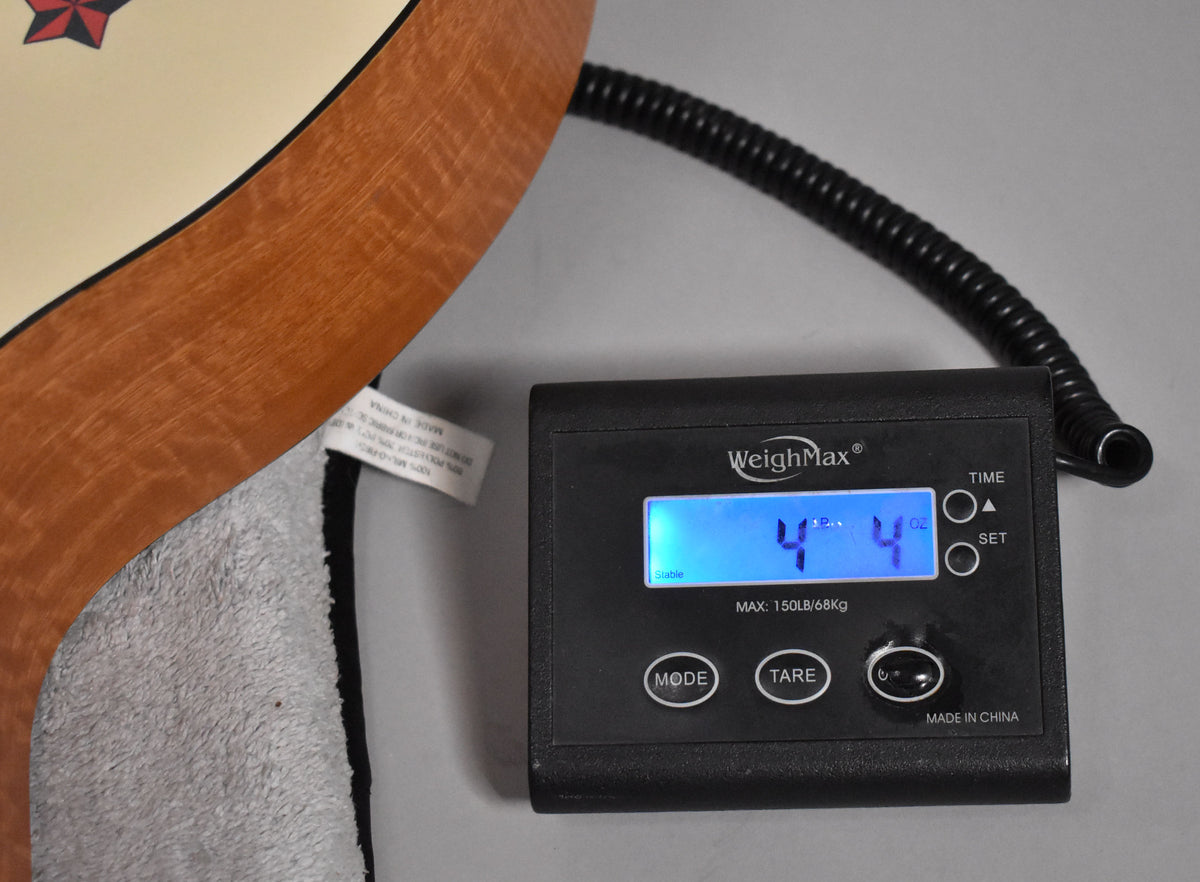 The guitar's light brown wood side is visible, resting on a gray towel, next to a black digital scale displaying "4 lbs 4 oz".