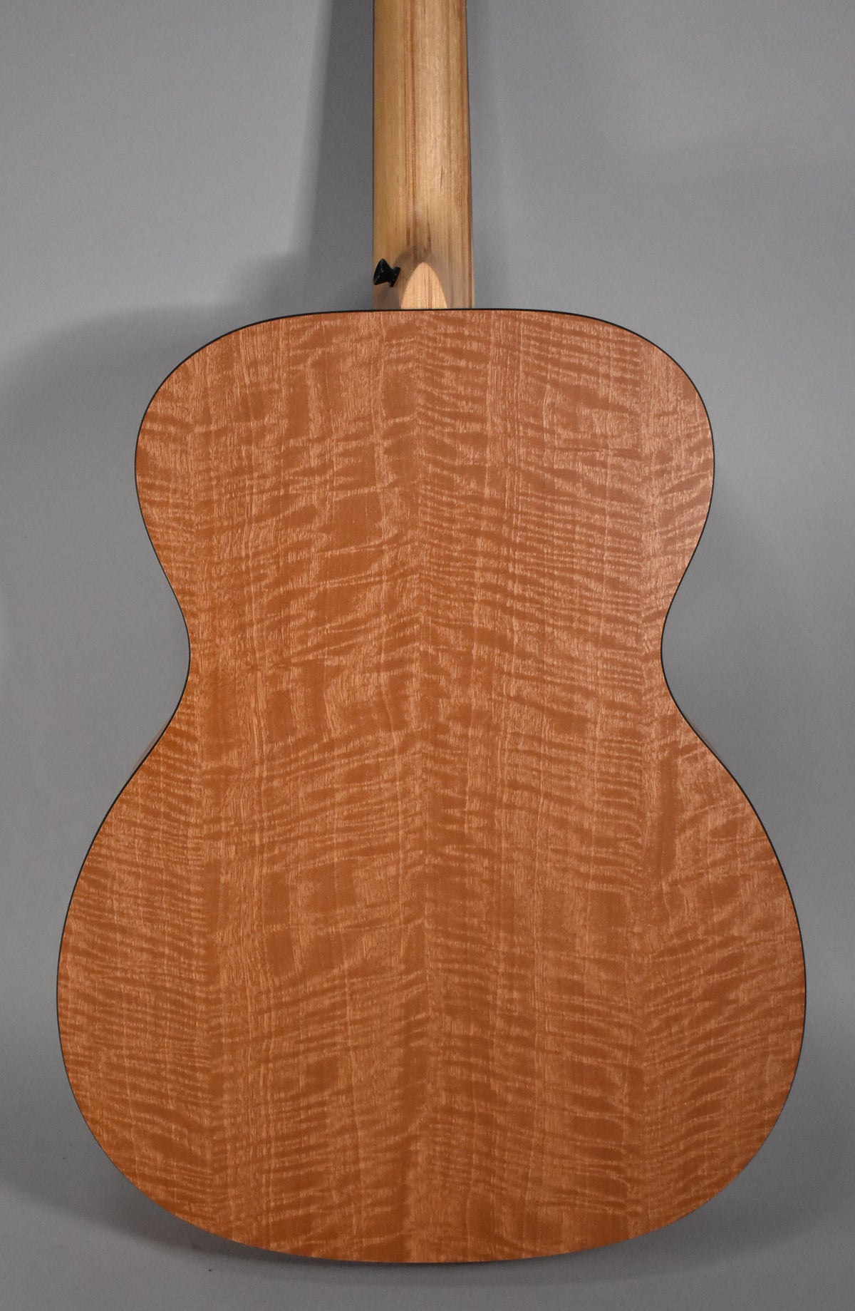 The back of the acoustic guitar, showing a light brown, highly figured wood grain with a black binding and a light wood neck.
