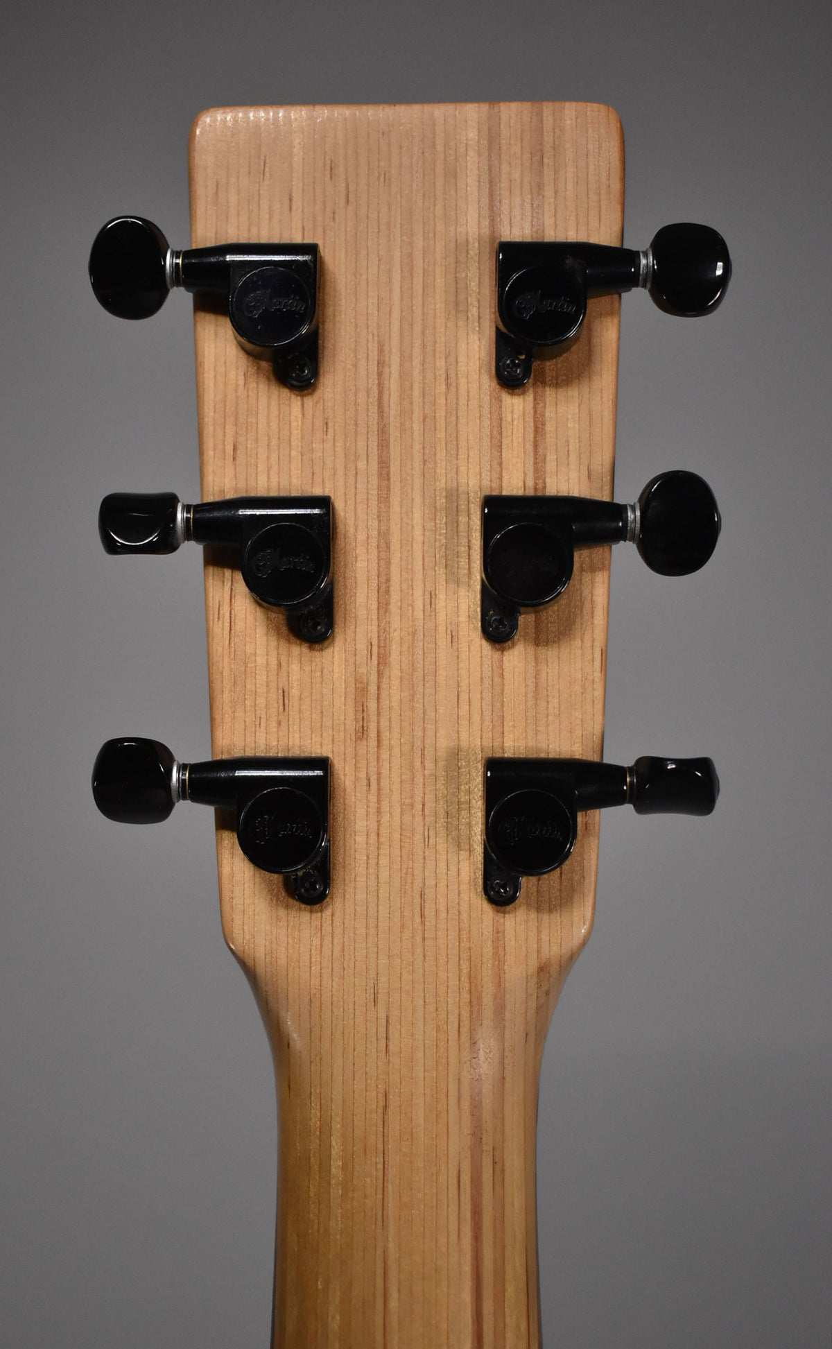 The back of the guitar's headstock and neck, showing six black tuners on a light wood grain, with minor wear on the neck.