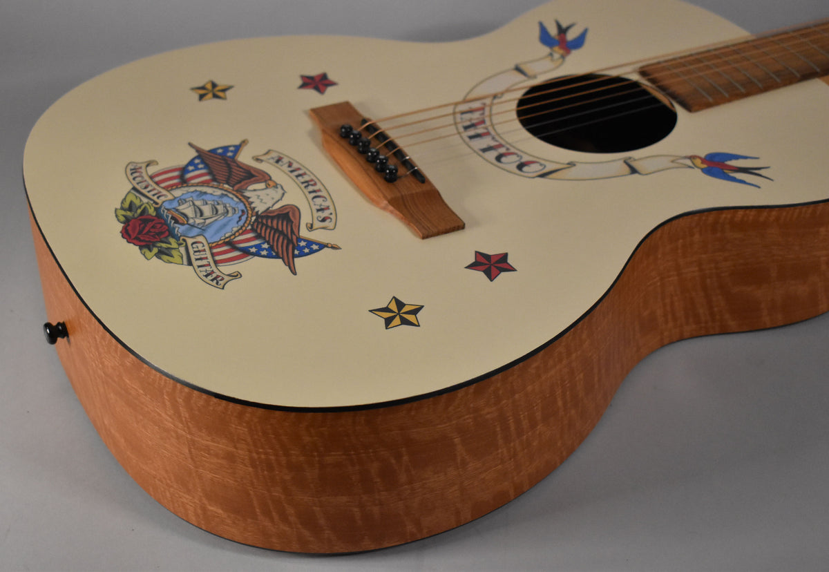The cream-colored acoustic guitar body, with a natural wood grain side, is adorned with colorful tattoo-style decals.