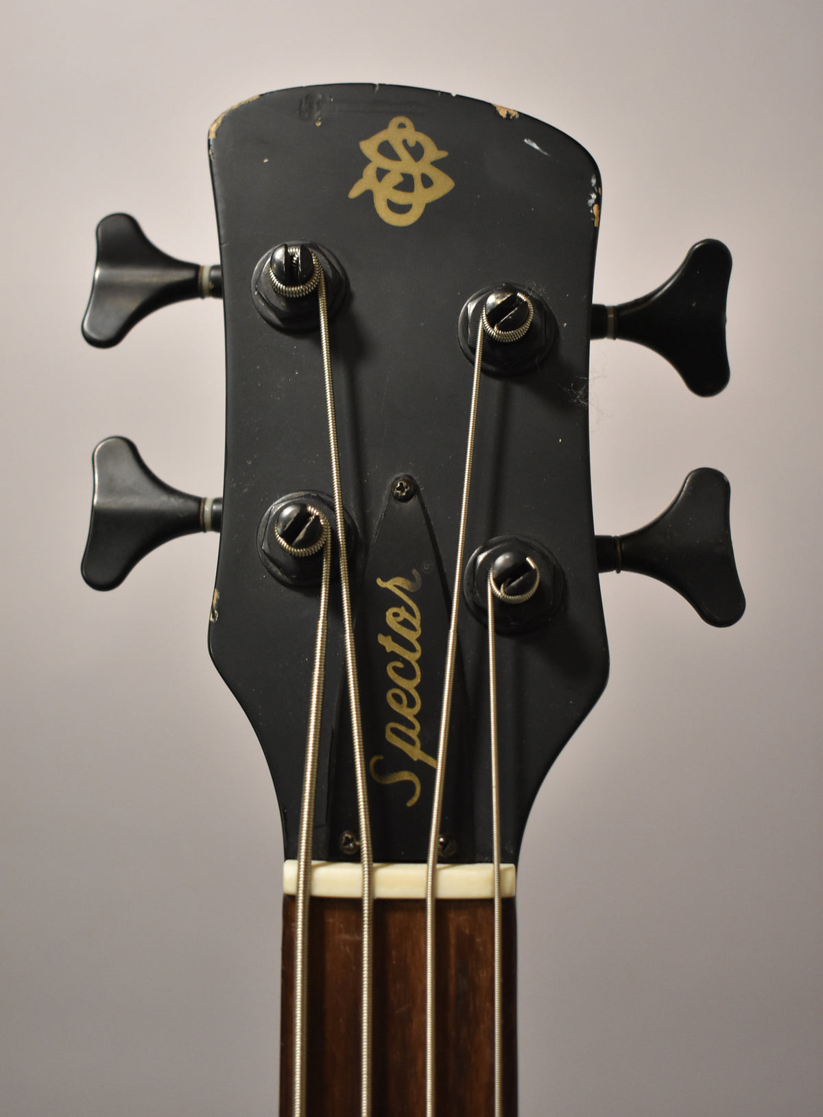 Close-up of the matte black headstock, showing four black tuning pegs, a gold logo, and visible wear on the top edge.