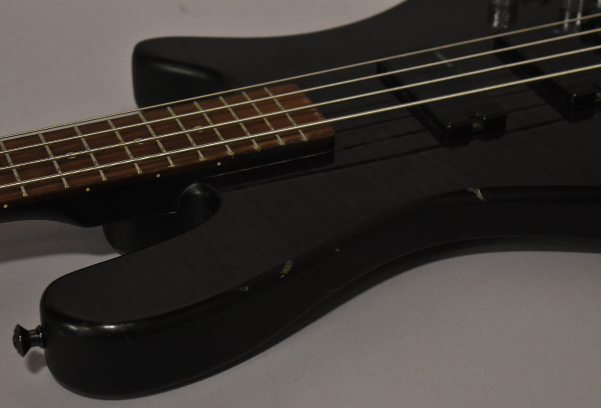 Close-up of the matte black bass body and lower neck, showing a few small chips and scratches on the finish.