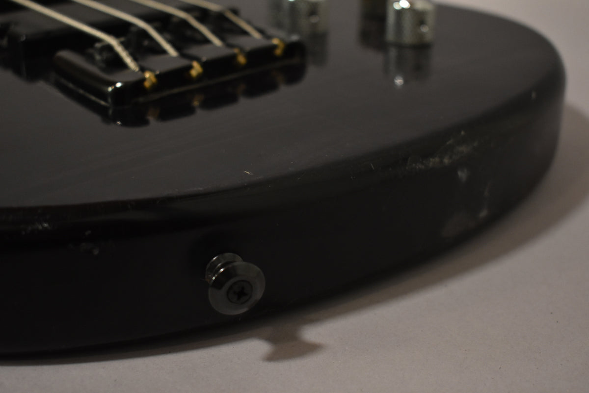Close-up of the bass body's lower bout, showing the matte black finish, black strap button, and visible scuffs and wear on the edge.
