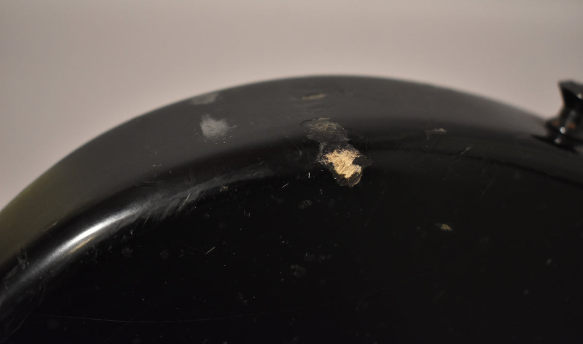 Close-up of the bass body's upper curve, showing heavy wear, chips, and scratches on the matte black finish, revealing lighter wood underneath.