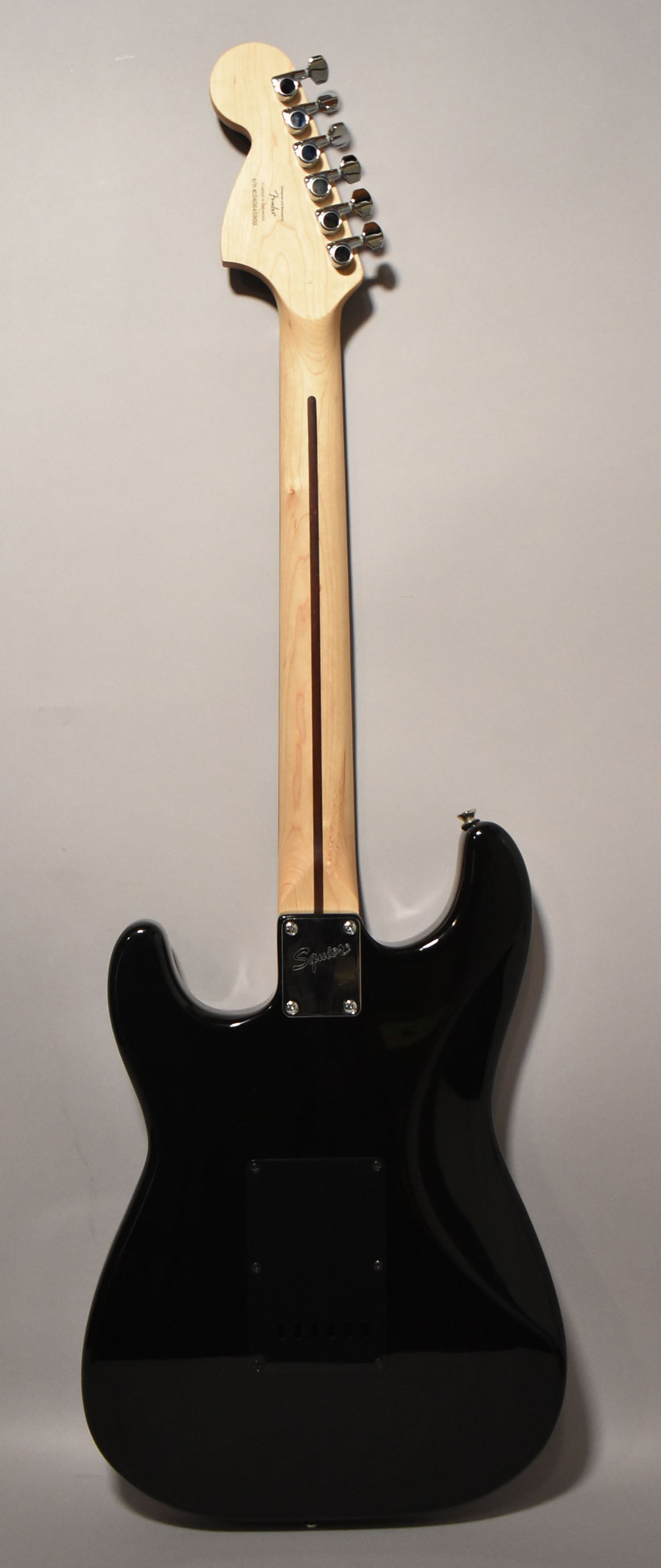 Full rear view of a glossy black Stratocaster with a light maple neck, chrome tuners, and a black tremolo cover.