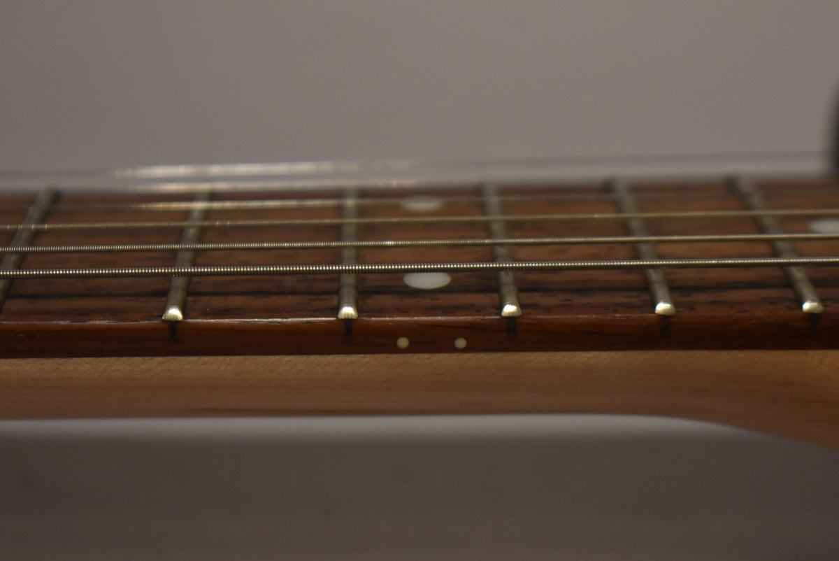 Close-up of the guitar's dark fretboard and strings, showing white dot inlays and two small side dots on the light wood neck.