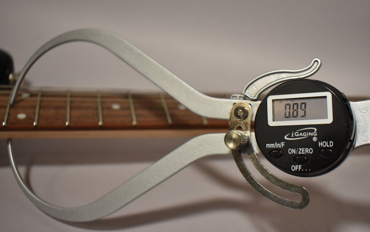 A digital caliper measures the fretboard radius, showing 0.89, with the guitar's dark brown fretboard and frets visible behind it.