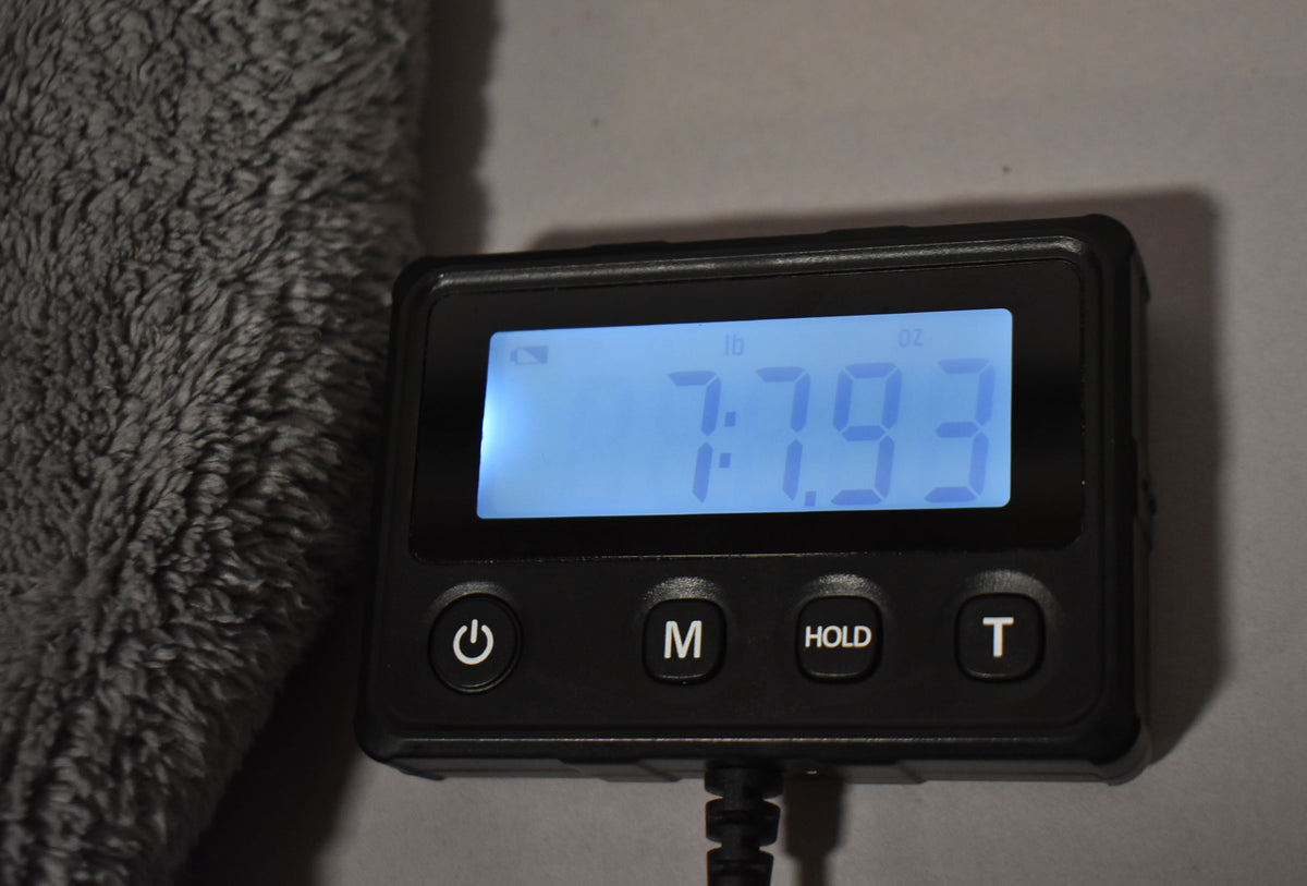 A digital scale displays "7 lb 7.93 oz" with a fuzzy grey object partially visible on the left.