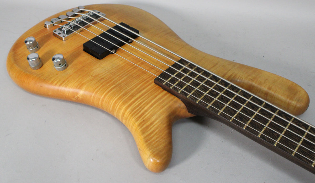 The upper body of a natural transparent satin bass, showing three chrome control knobs, a black pickup, and the dark fretboard.