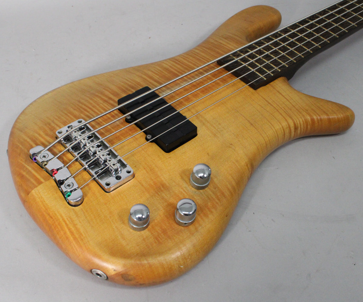 Close-up of the bass body, showing the natural wood grain, chrome bridge with colored string ends, black pickups, and three chrome knobs.