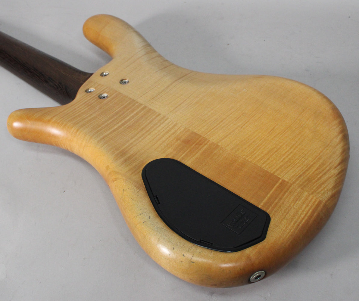 The bass's natural transparent satin finish back shows wood grain, a black control cavity cover, and light wear near the output jack.