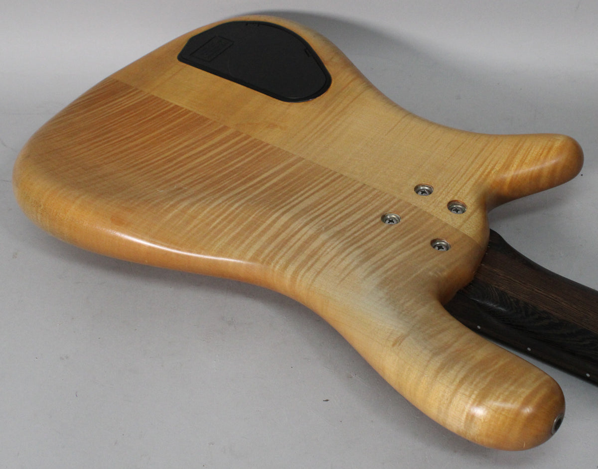 The bass's natural transparent satin finish body, with prominent wood grain, is seen from the back, showing the neck joint and control cavity.