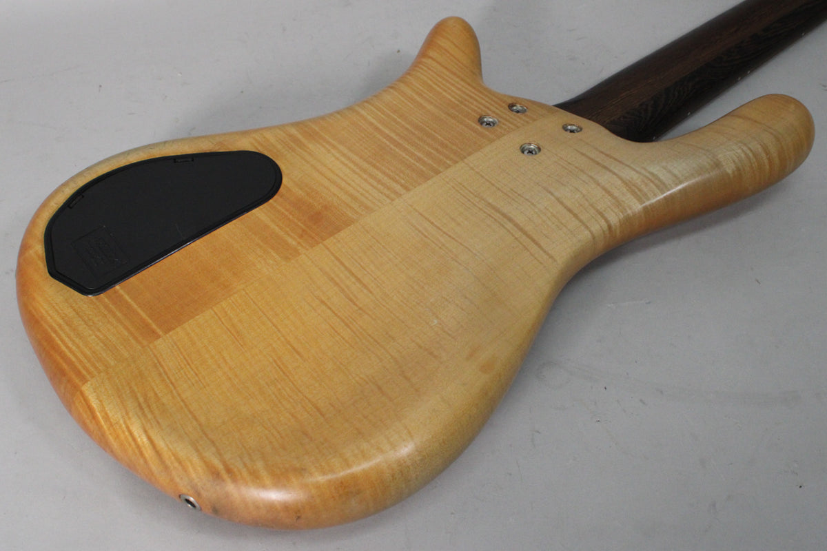 The bass's natural transparent satin finish body, with prominent wood grain, is seen from the back, angled to show the neck joint and black control plate.