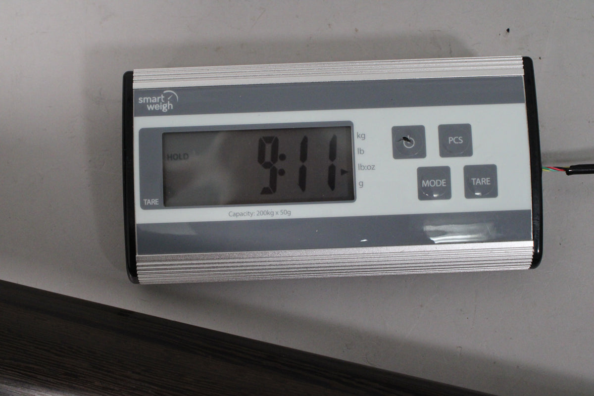 A digital scale displays "9.11" in large black numbers, likely indicating the bass's weight, with a dark wood grain visible below.