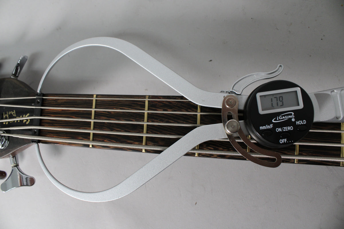 The bass's dark wood fretboard is shown with a digital caliper measuring the string height at 1.79mm.