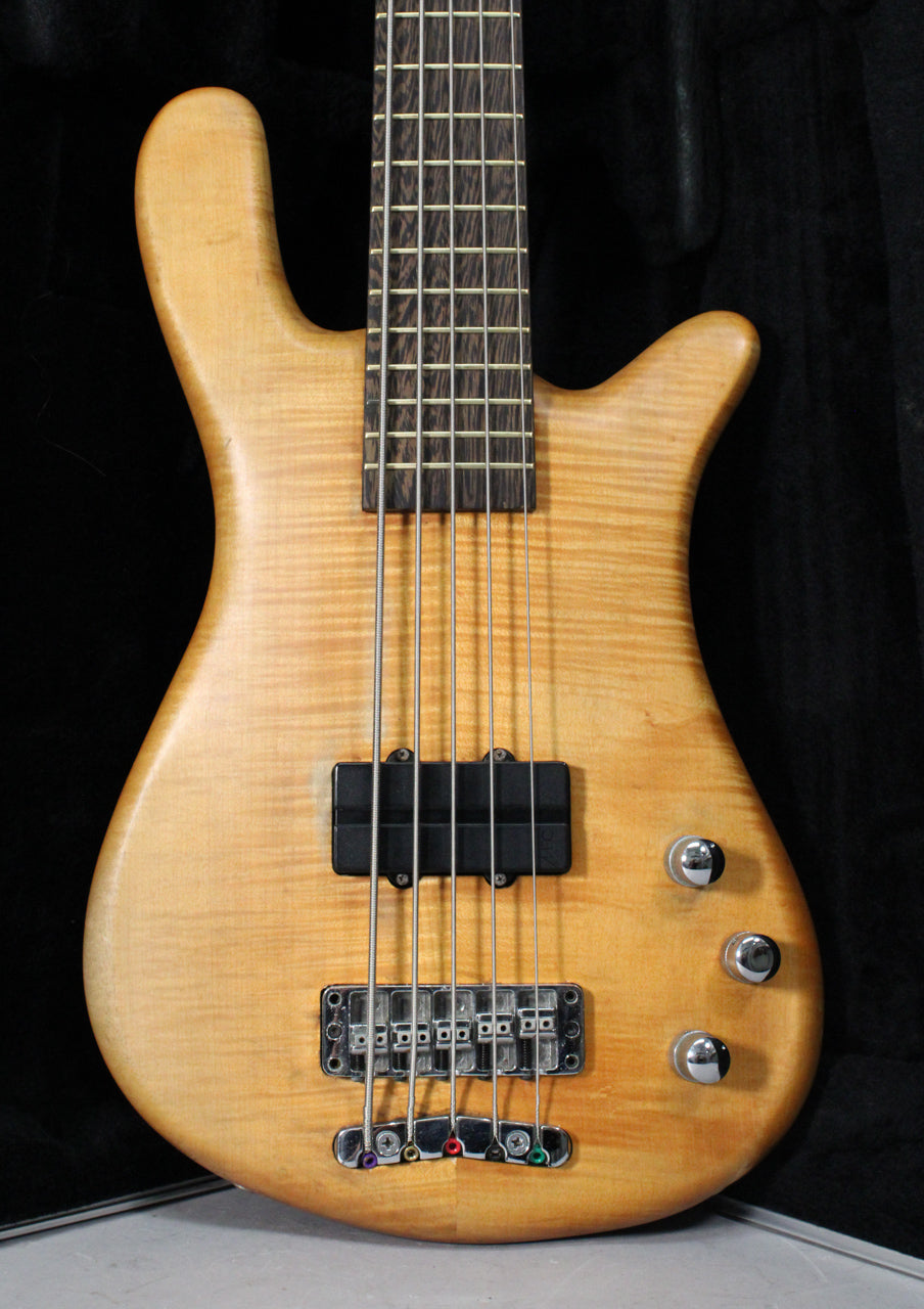 The bass guitar's upper body and neck are visible, showing a natural transparent satin finish with flame maple grain, black pickups, and three chrome knobs.