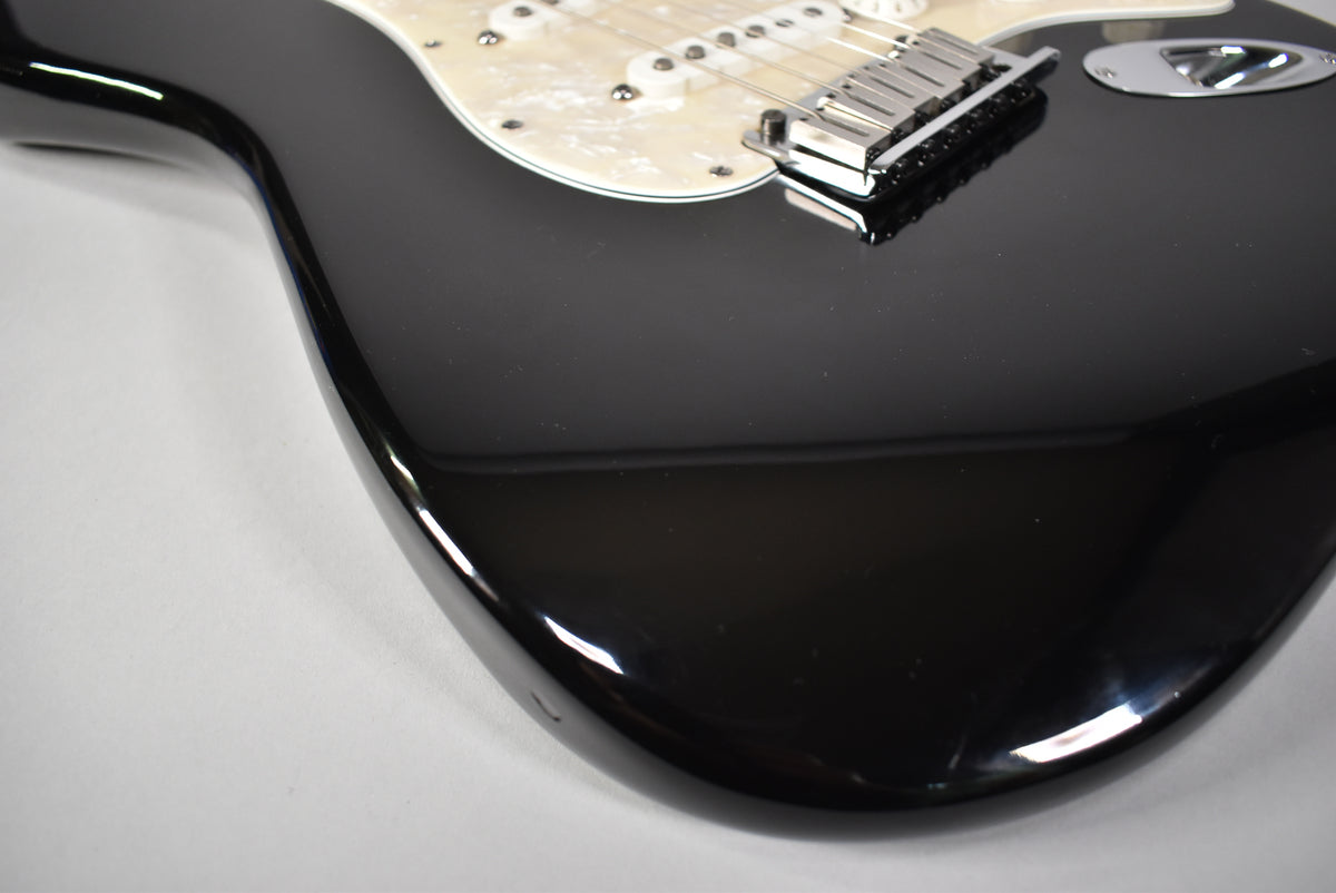 Upper body of a glossy black Stratocaster, angled from the lower bout, showing a pearloid pickguard and chrome bridge.