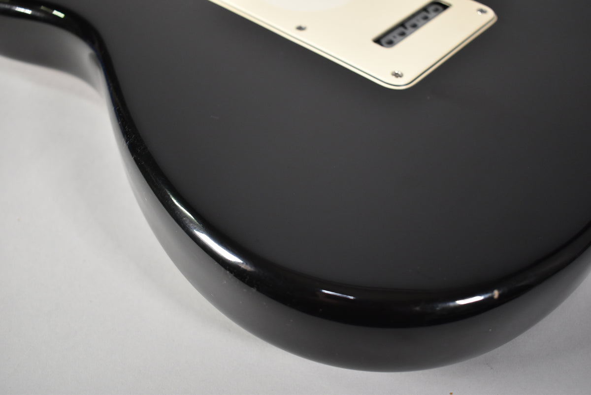 Close-up of the guitar's lower bout, showing the glossy black finish with minor edge wear and a cream pickguard with visible screws.