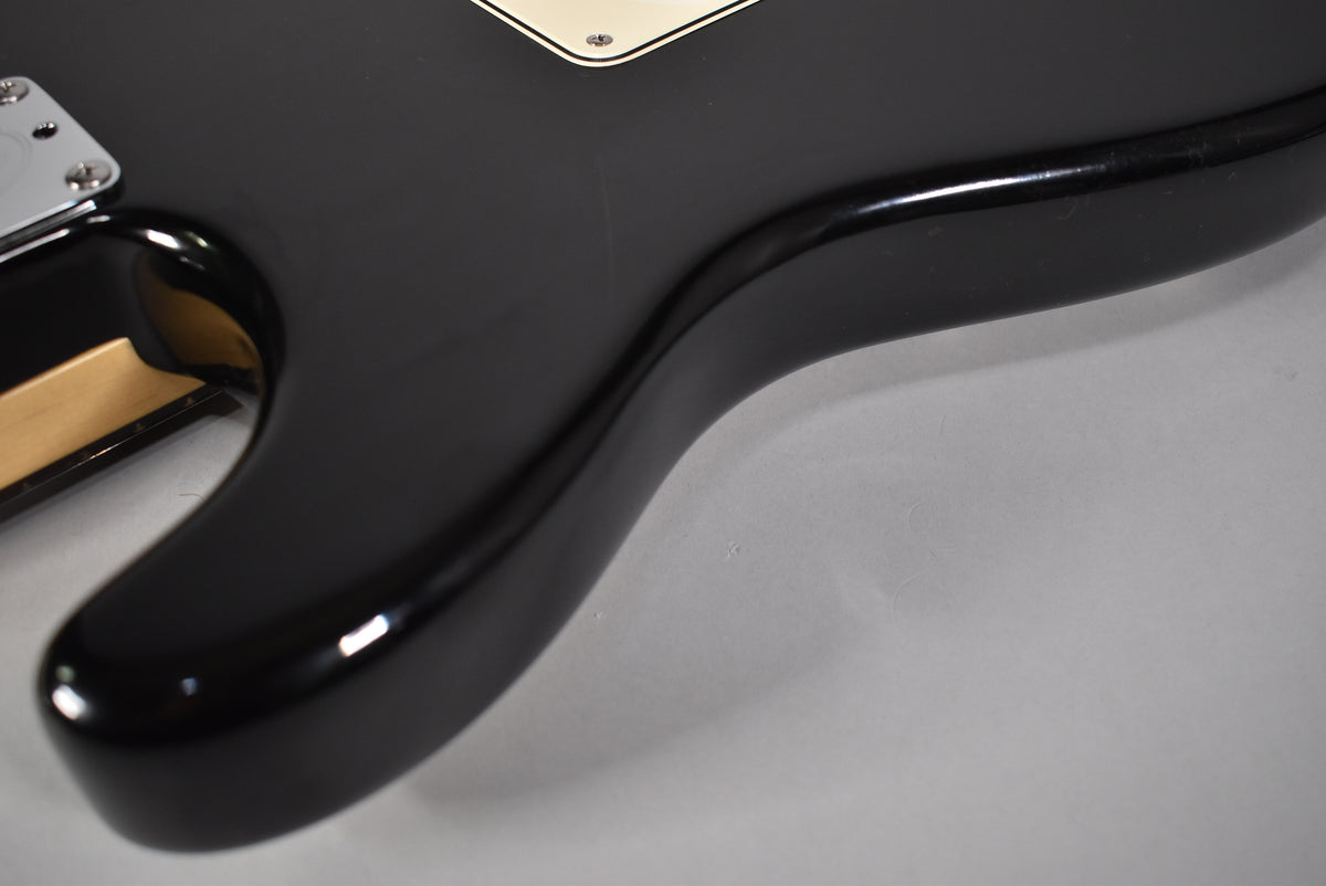 Close-up of the black gloss body's lower horn and cutaway, showing light scratches and a glimpse of the maple neck heel.