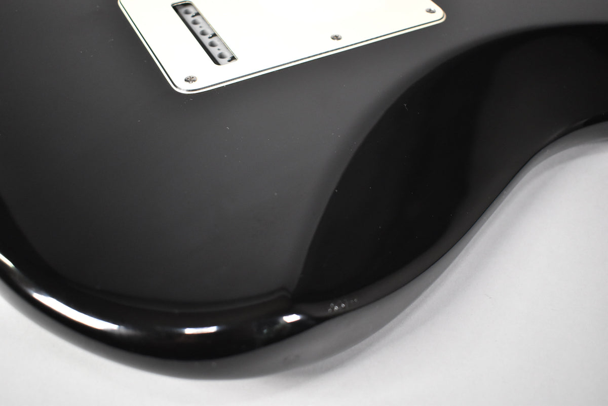 Close-up of the guitar's lower body, showing the black gloss finish, white tremolo cover, and a small ding on the lower bout.