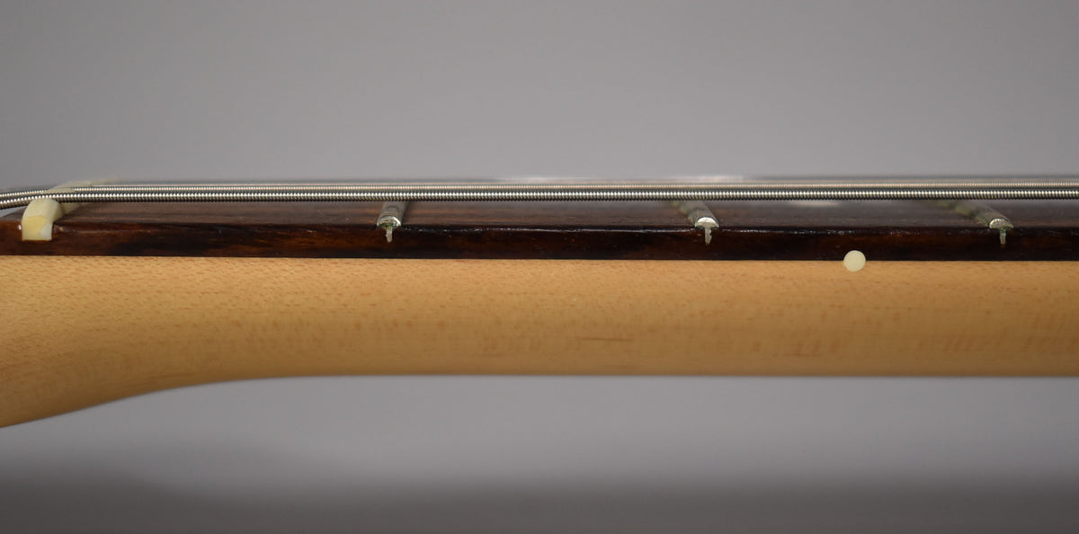 Close-up of the guitar's neck, showing the dark rosewood fretboard, light maple neck, and a small white dot inlay.