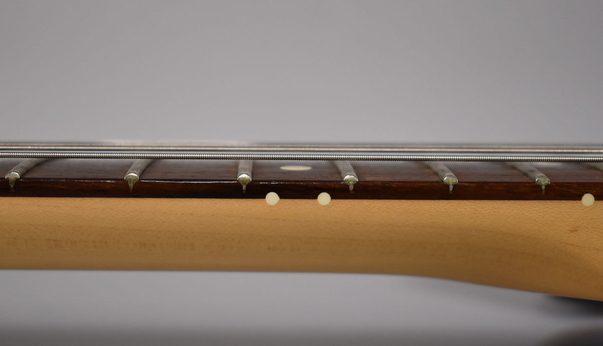 Close-up of the rosewood fretboard and maple neck, showing the frets, strings, and two white side dot markers.